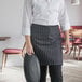 A woman in a black and white pinstripe half bistro apron holding a plate.