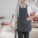 A woman wearing a black and white pinstripe bib apron with three pockets in a professional kitchen.