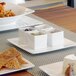 A table with white square Front of the House ramekins filled with different colored food.