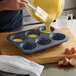 A person pouring batter into a Fox Run fluted jumbo muffin pan.