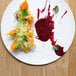 A Front of the House white porcelain round flat plate with food and a sauce on it on a wood table.