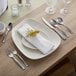 An Acopa stainless steel dinner knife next to a plate with a flower on it.