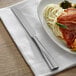 An Acopa stainless steel dinner knife on a plate of food on a table.