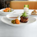 An Ellipse white porcelain oval coupe plate with a bacon wrapped steak and greens on top.