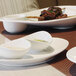 A close-up of a Front of the House white oval porcelain coupe plate with meat on it.