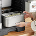 A person holding a Vollrath stainless steel steam table pan full of food.