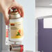 A hand using a Rubbermaid Mandarin Orange air freshener refill to spray air freshener in a room.