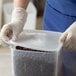 A person wearing gloves putting a Carlisle translucent plastic lid on a container of chocolate chips.