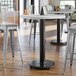 A Lancaster Table & Seating bar height table base with FLAT Tech Equalizer levelers on a wood floor.