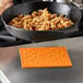 An orange Lodge silicone trivet under a black pan of food.