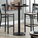 A Lancaster Table & Seating bar height table base with a glass top and two chairs.