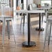 A Lancaster Table & Seating bar height table base with table equalizers and stools in a room.