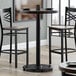 A Lancaster Table & Seating bar height table with a glass top on it and two chairs.