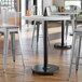 A white round table with a Lancaster Table & Seating cast iron bar height table base.