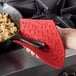 A hand holding a Lodge red silicone trivet over a pan of food.