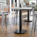 A Lancaster Table & Seating bar height table base with self-leveling feet on a white table in a room.
