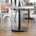 A Lancaster Table & Seating cast iron table base with self-leveling feet and a spider attachment on a white table with a black top.