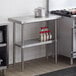A Regency stainless steel work table with undershelf in a kitchen with a stove and pot on a shelf.
