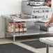 A man in a professional kitchen using a Regency stainless steel equipment stand with an undershelf to hold a metal container.