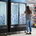 A woman looking at an Avantco indoor glass door ice merchandiser in a grocery store aisle.