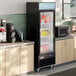 A black swing glass door merchandiser freezer with LED lighting, stocked with frozen food items and positioned between countertops in a commercial setting.