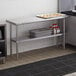 A Regency stainless steel work table with an undershelf holding metal containers.