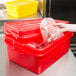 A hand holding a plastic bag of meat in a red Vollrath food storage container.