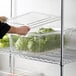 A person using a Cambro food storage box with a colander to hold vegetables.