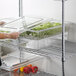 A woman using a Cambro clear plastic container to put food in a colander.