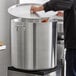 A man pouring meat into a Choice Heavy Weight Aluminum Stock Pot on a stove in a professional kitchen.