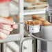 A person holding a Tablecraft stainless steel measuring cup over a bowl of brown granules.