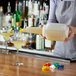 A woman using a Vollrath white plastic pour container to pour a yellow drink into a glass.