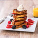 A stack of Rich's French Bread French toast with whipped cream and berries on a plate.