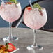 Two Arcoroc gin and tonic glasses filled with pink drinks and garnished with fruit and herbs.