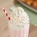 A glass of pink milkshake topped with Rich's On Top whipped cream and a straw.