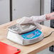 A person in a white glove cleaning an AvaWeigh waterproof digital portion scale.