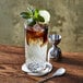 An Arcoroc beverage glass filled with iced tea and limes on a coaster.