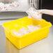A hand putting a plastic bag of chicken in a yellow Vollrath food storage container.