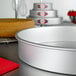 A round silver Fat Daddio's cake pan on a table.