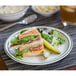 A Tuxton Emerald green speckle narrow rim china plate with a sandwich, pickles, and a glass of juice.