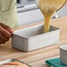A rectangular anodized aluminum bread loaf pan being filled with batter.