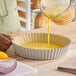 A round, deep fluted tart or quiche pan with a removable bottom being filled with a yellow liquid mixture.