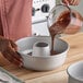 A person pouring cake batter into a Fat Daddio's ProSeries anodized aluminum ring cake pan on a wooden countertop.