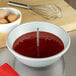 A stainless steel Fat Daddio's cake pan heating core rod sitting on a counter next to a bowl of red liquid with a whisk.