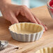 A small round fluted tartlet or quiche pan with a removable bottom, partially filled with dough.