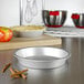 A silver Fat Daddio's ProSeries pie pan on a counter with red and yellow apples and cinnamon sticks.