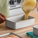 A rectangular anodized aluminum bread loaf pan being filled with batter.