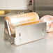 A Bulman stainless steel countertop film dispenser holding a roll of plastic wrap on a counter.