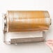 A hand inserting a roll of plastic wrap into a Bulman stainless steel countertop or wall mount film dispenser.