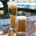 Two Arcoroc SAN plastic beer mugs filled with beer on a table.